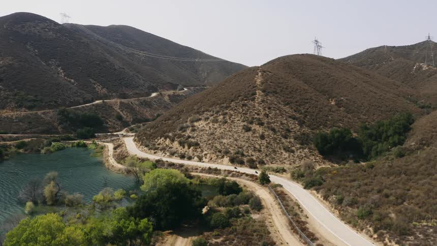 Two people drive motorcycles through the hills on the shore