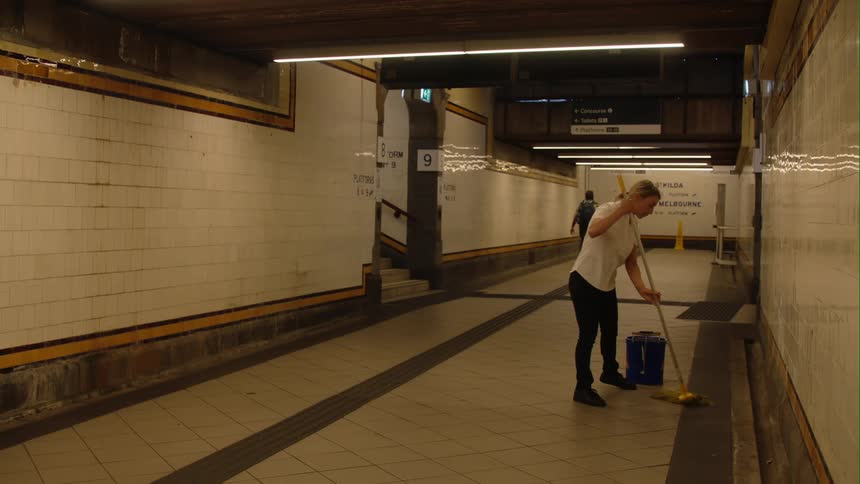 People are walking down a hallway as a woman is mopping the floor