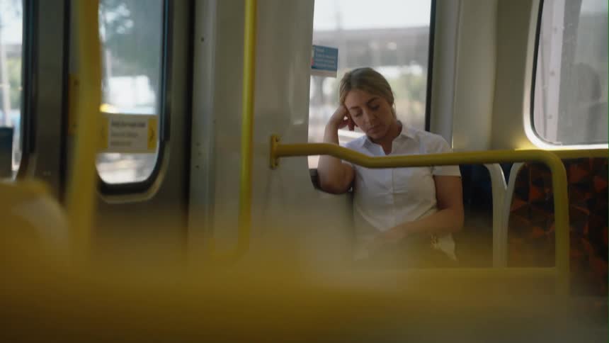 A woman sitting on a bus is napping with her head resting on her hand