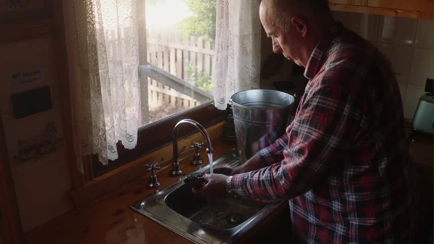 Old man takes daily catch of fish from pail and washes it in kitchen sink