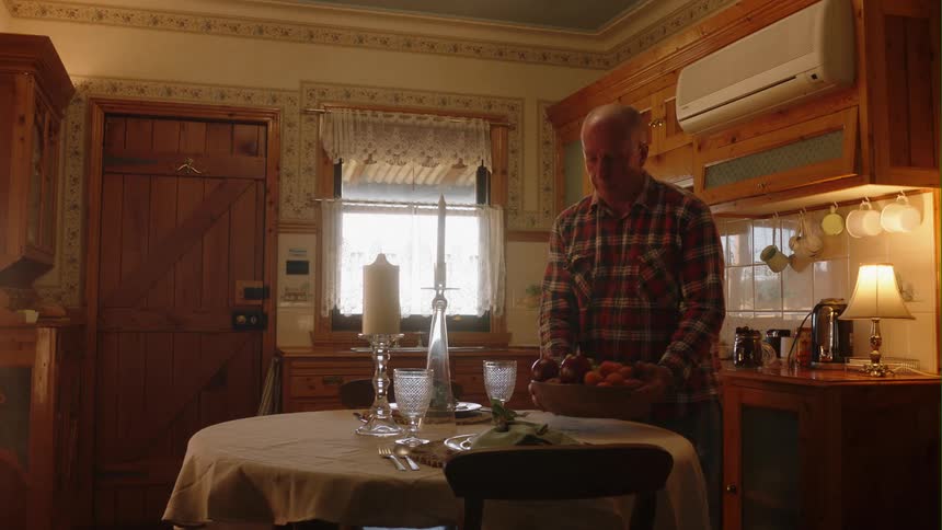 Elderly man brings a fruit bowl to the table in the kitchen at home