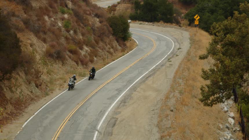 Two people are riding motorcycles through a rural area