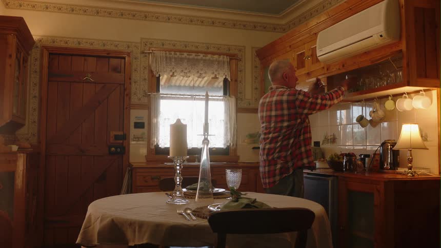 In kitchen older man sets the table with glassware