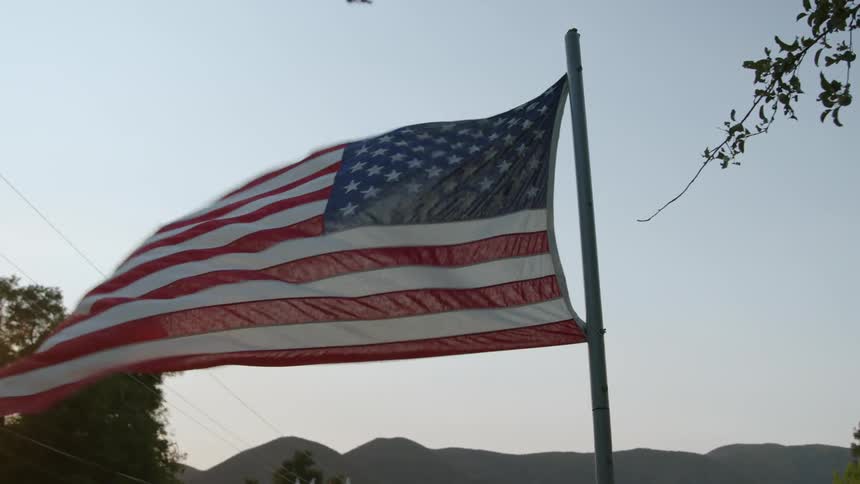 Tattered american flag flaps in the breeze with misty mountains in the background