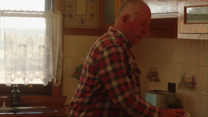A man places a bowl of fruit on his kitchen table