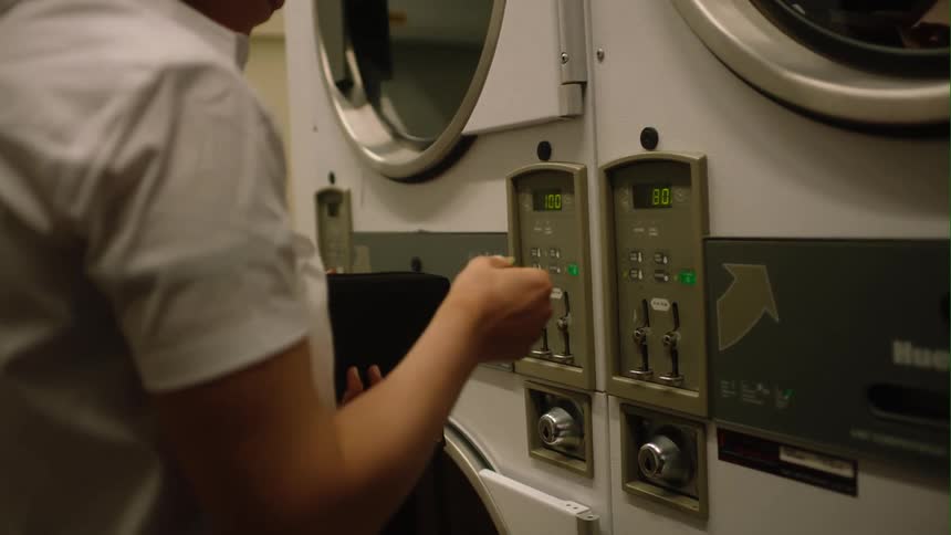 Woman puts coins into laundry machine at the laundromat