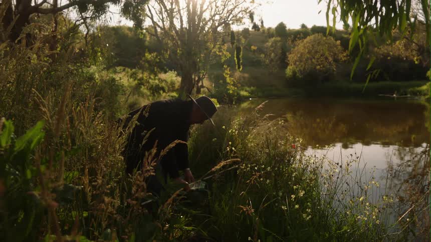 A man is fishing on a pond during sunset