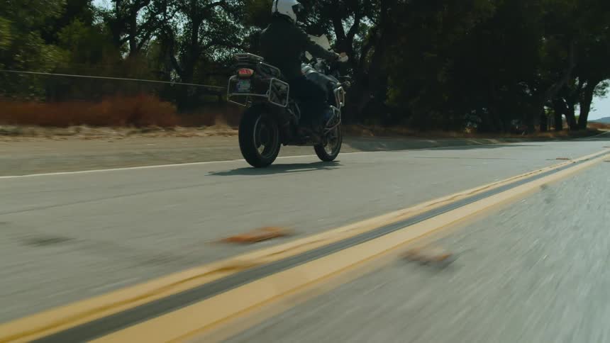 Motorcyclist rides motorcycle along country highway toward mountains on the horizon