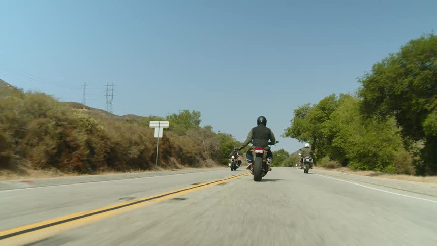 Motorcyclist greets another motorcyclist traveling the opposite way via gesture as they travel along highway in countryside