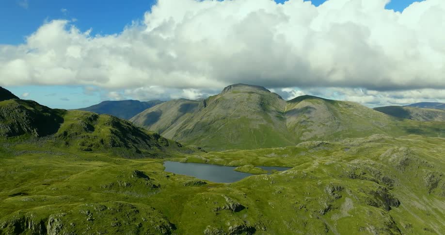 Green hills and mountains surround lake under a cloudy sky