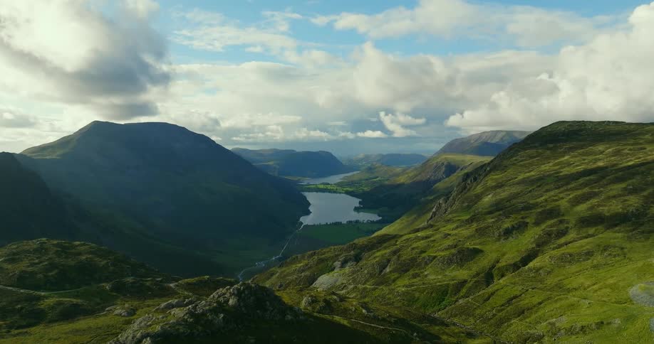River winds into lake in misty valley surrounded by green hills and mountains under a cloudy sky