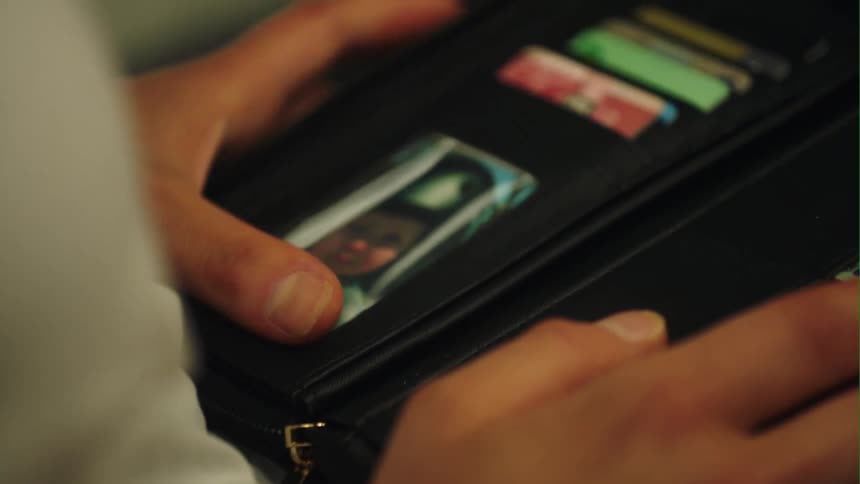 Woman looks down at photograph in black leather purse with credit cards