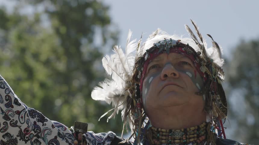 A native man with feathers in his hair looks up at the sky