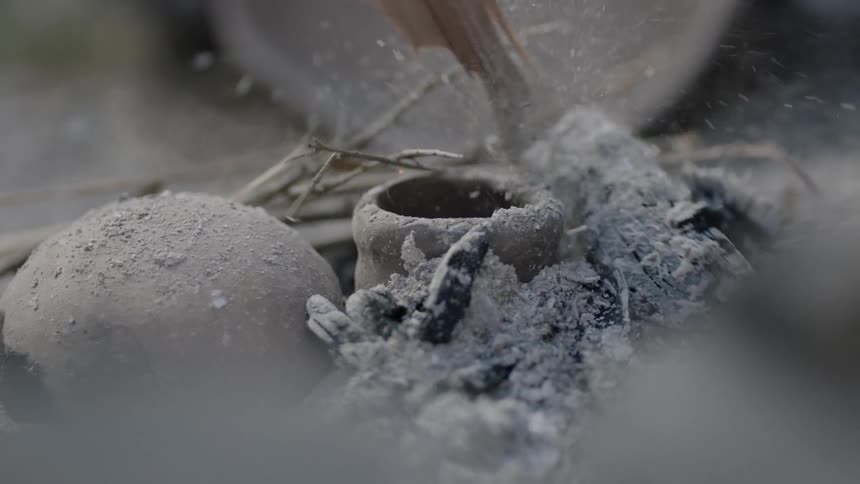 Person using a stick to stir ashes near a recently extinguished fire