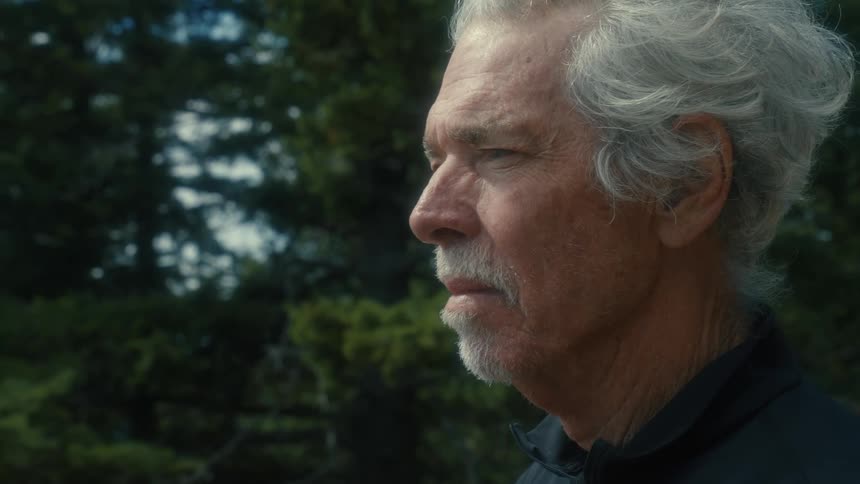 A man standing outside squinting a bit as he looks at nature