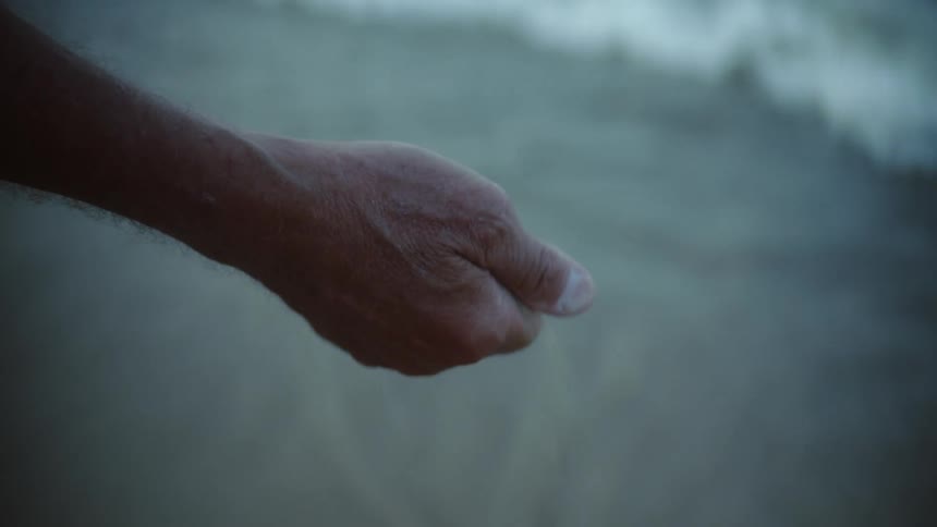 Sand falls through a mans fingers as he makes a fist while standing on the beach