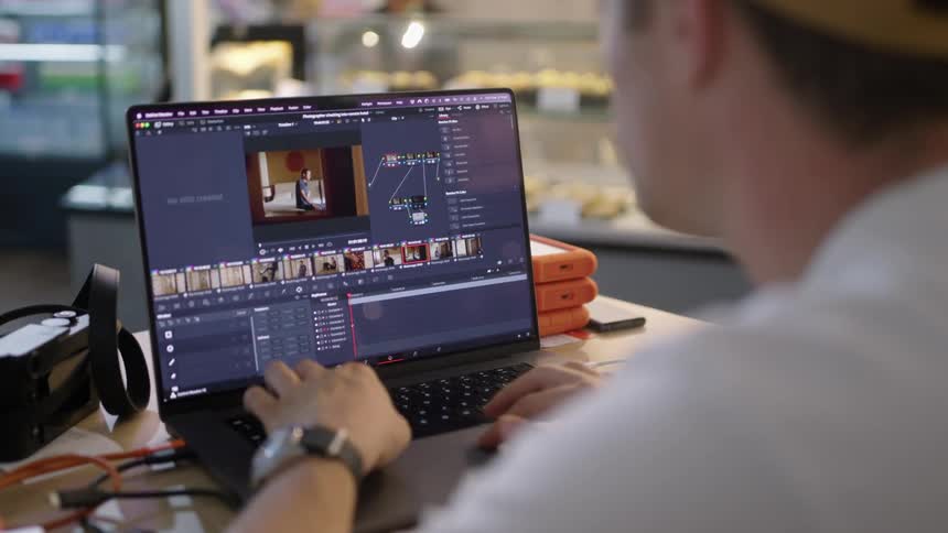 Photographer sits at table in restaurant using photo editing software on a laptop