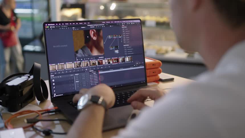 A man in a shop works on a computer as he crops a photo while a woman browses display cases