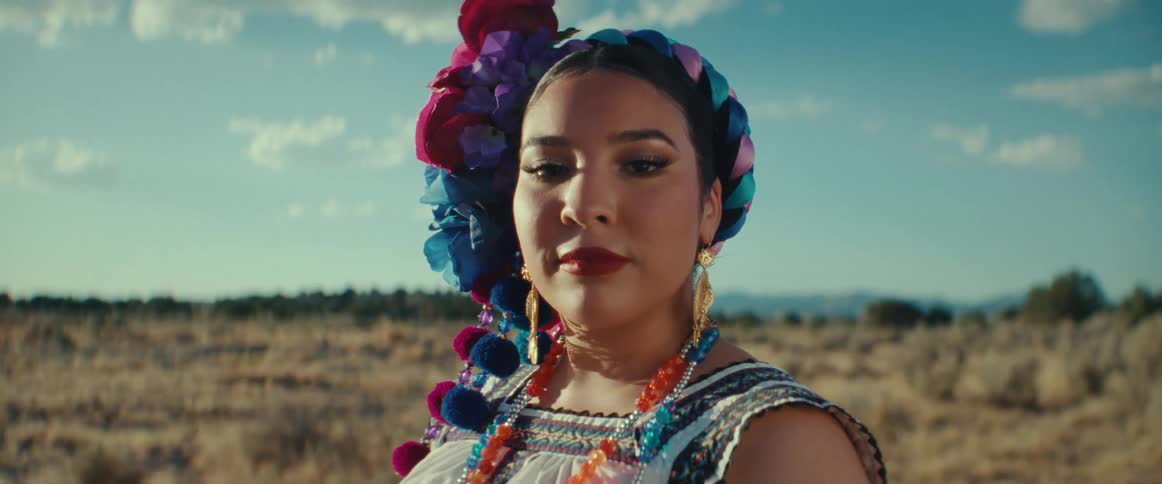 A woman wearing a traditional costume stands in a field looking into the camera