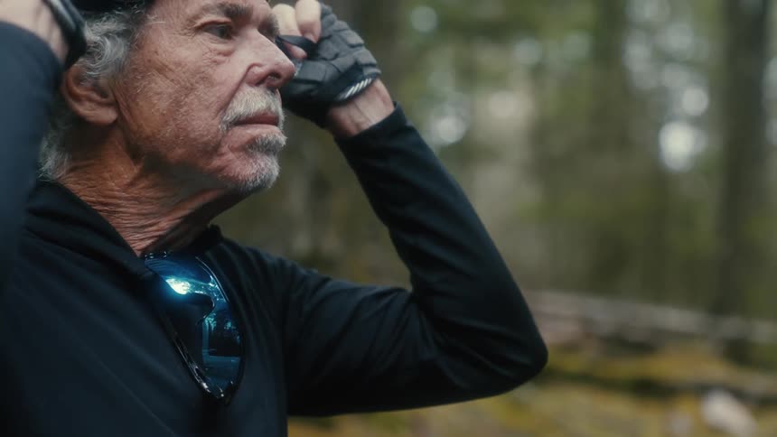 A man puts on a bicycle helmet while standing in the woods