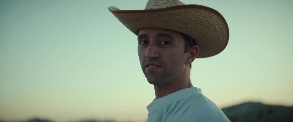 A portrait of a man standing outdoors wearing a cowboy hat