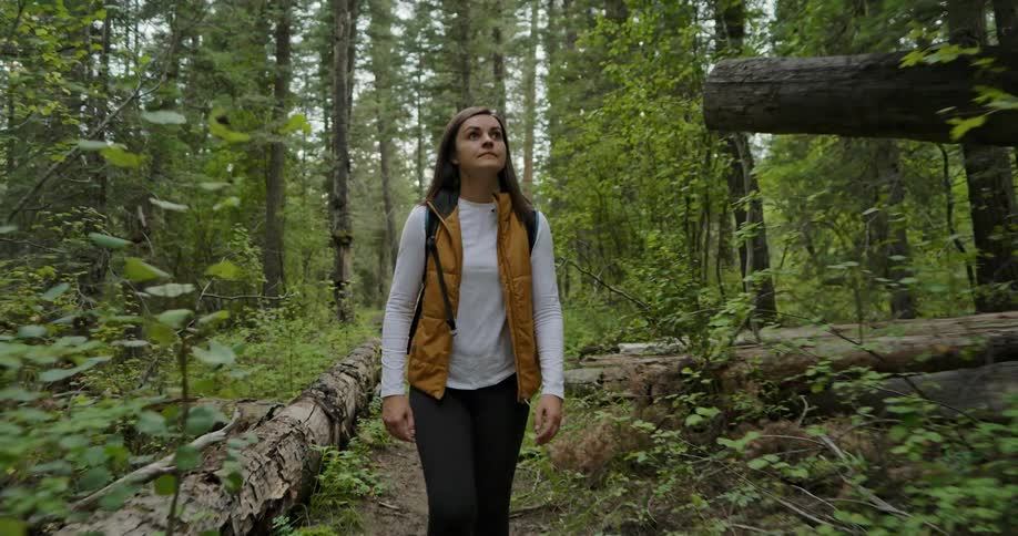 A woman walking on a trail through the woods moves a branch out of her way as she hikes past