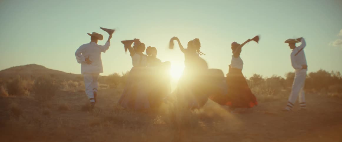 A group of men and women wave flags in the air as they dance outside