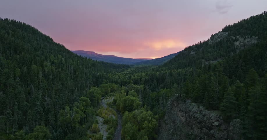 River runs through valley past cliffs tors and forested mountains toward red sky