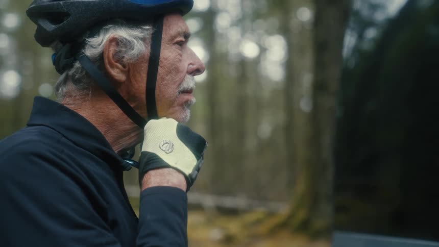 A man is standing outside with a helmet on his head as he adjusts the strap on his chin