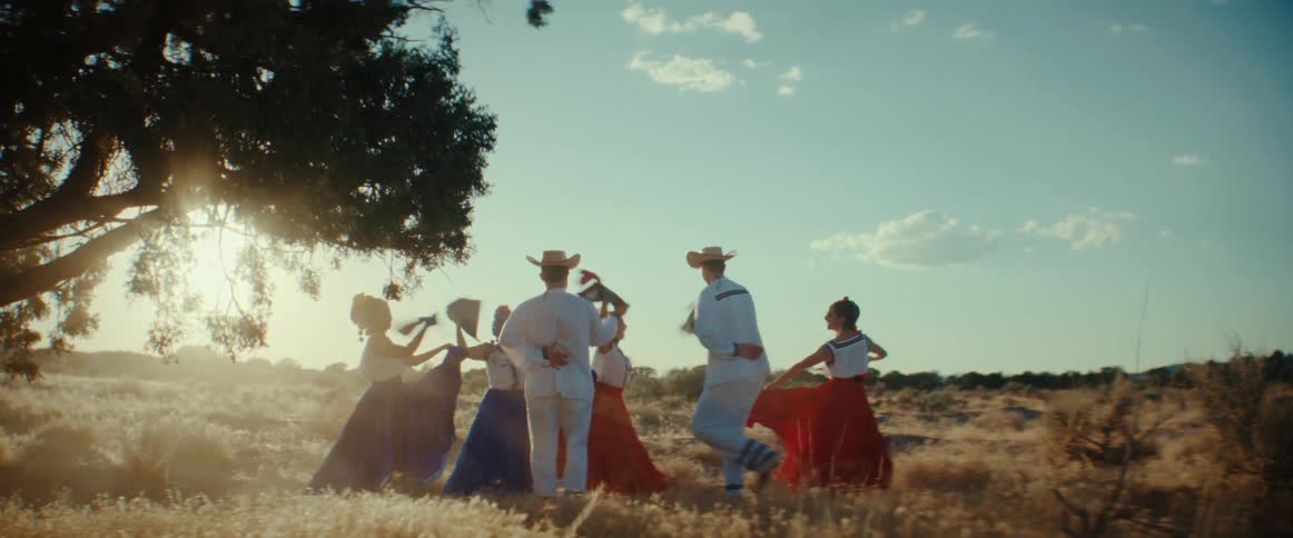 A group of Mexican folk dancers performing a dance outside near a tree