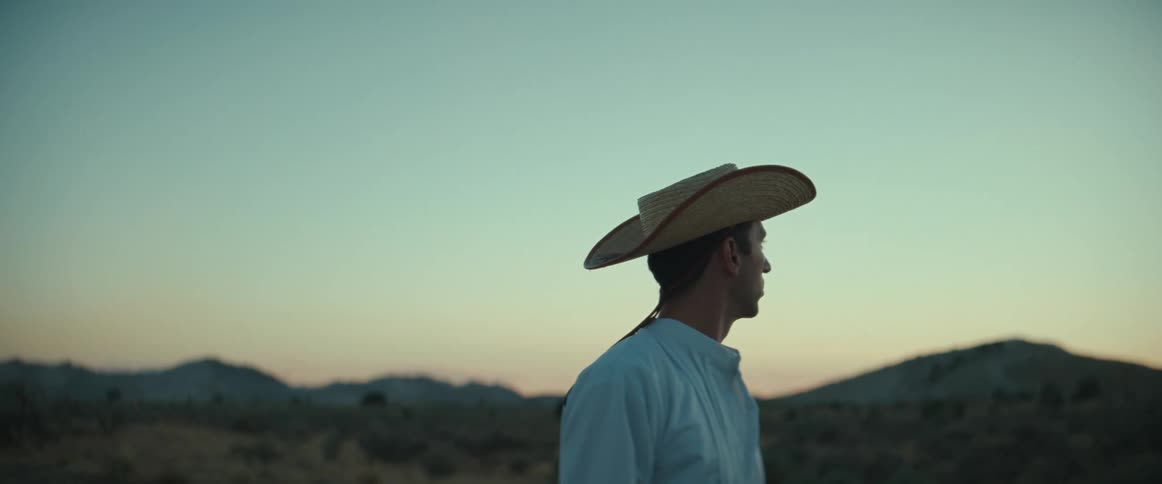 A man in a hat looks off into the distance at dusk
