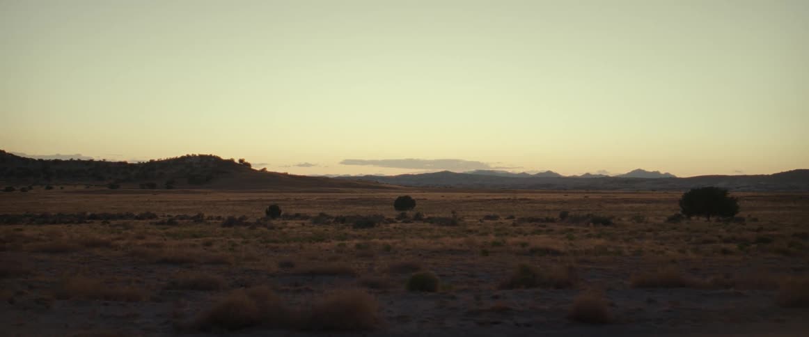 Plains stretch to mountains on the horizon under a slightly red tinted sky