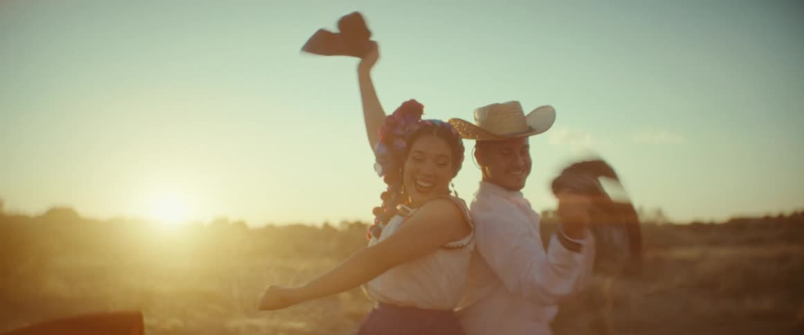 A group of people laugh and wave scarves while dancing in traditional clothing