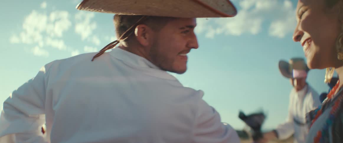 Hispanic dancers wave scarves while performing a traditional dance in a field