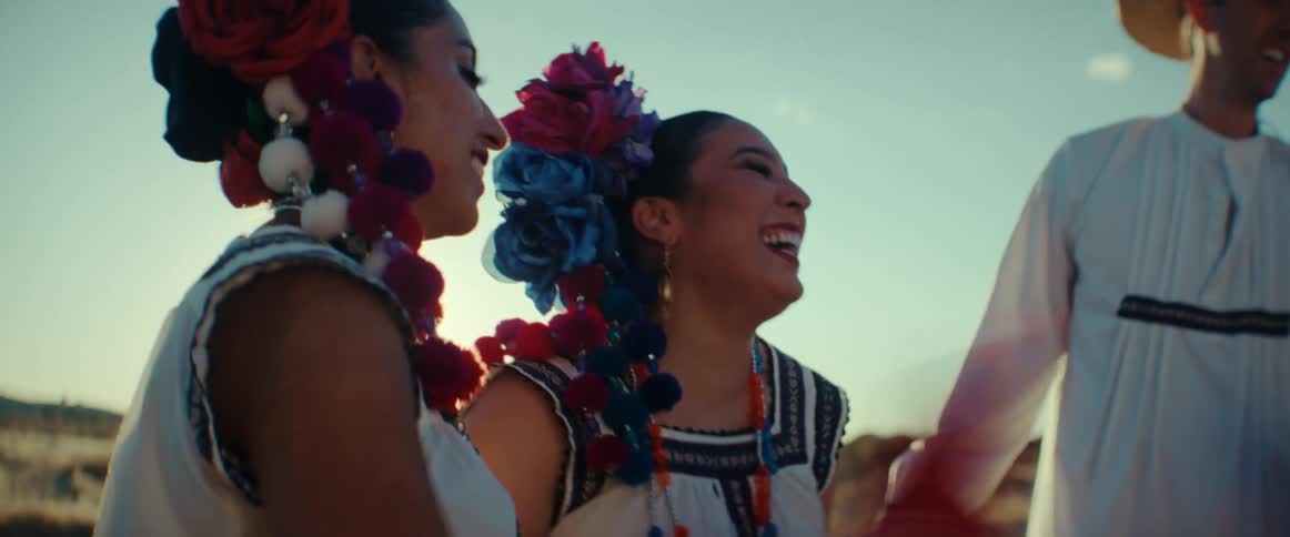Folk dancers stand in field on sunny day smiling and laughing