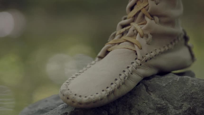 A person's boot is standing on a rock by the water