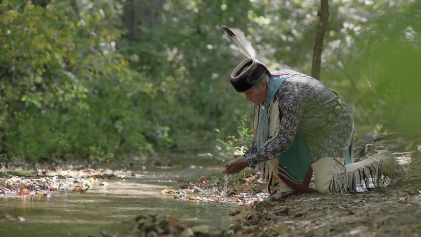 A man in native costume washes his hands in a stream