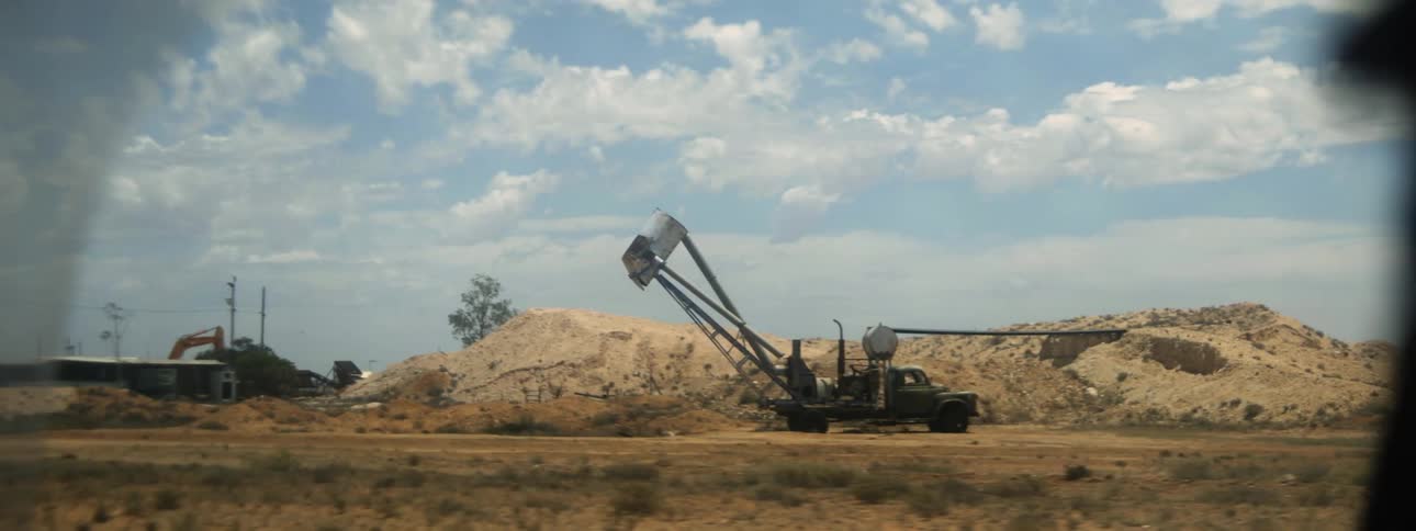 A man stands next to a bulldozer parked in a field by a large pile of rubble