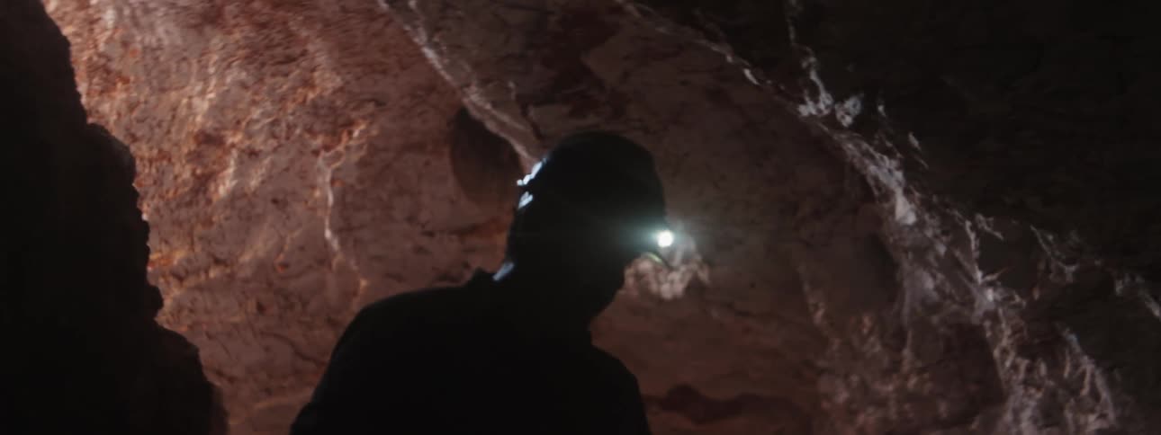 Miner wearing headlamp silhouetted against tunnel wall manuevers carefully