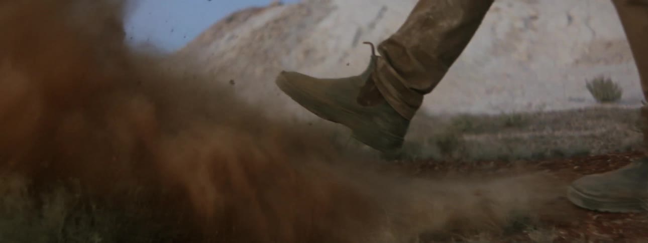 A man purposely kicks up dirt while walking through a canyon