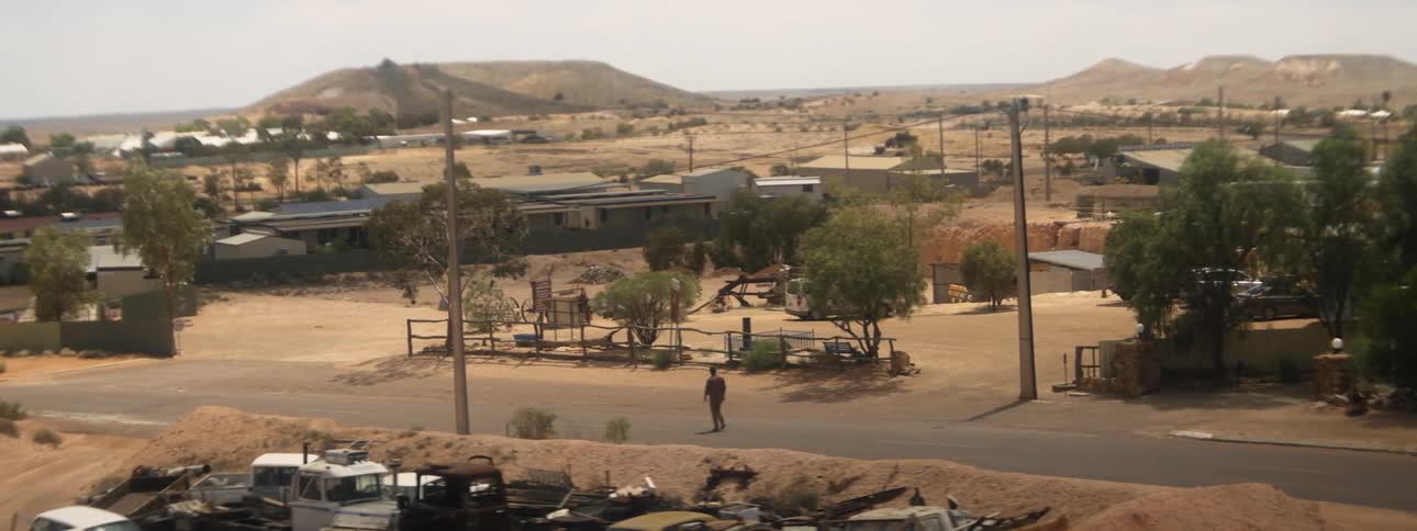 Man walks along road through small arid town in desert near hills