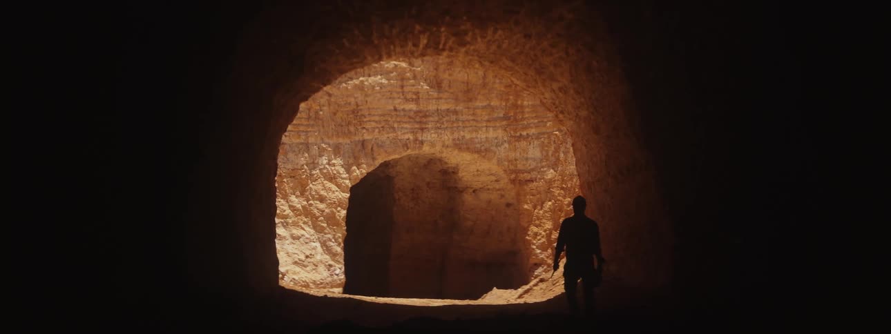 A silhouette of a man is seen as he is walking through a tunnel carved into sandstone