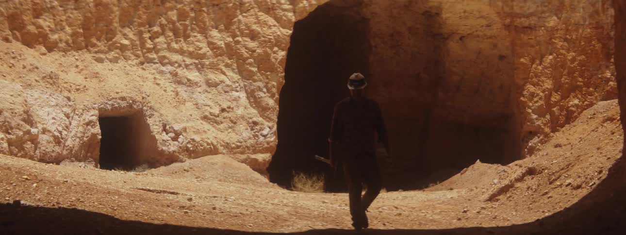 A man carrying a pick walks out of a cave