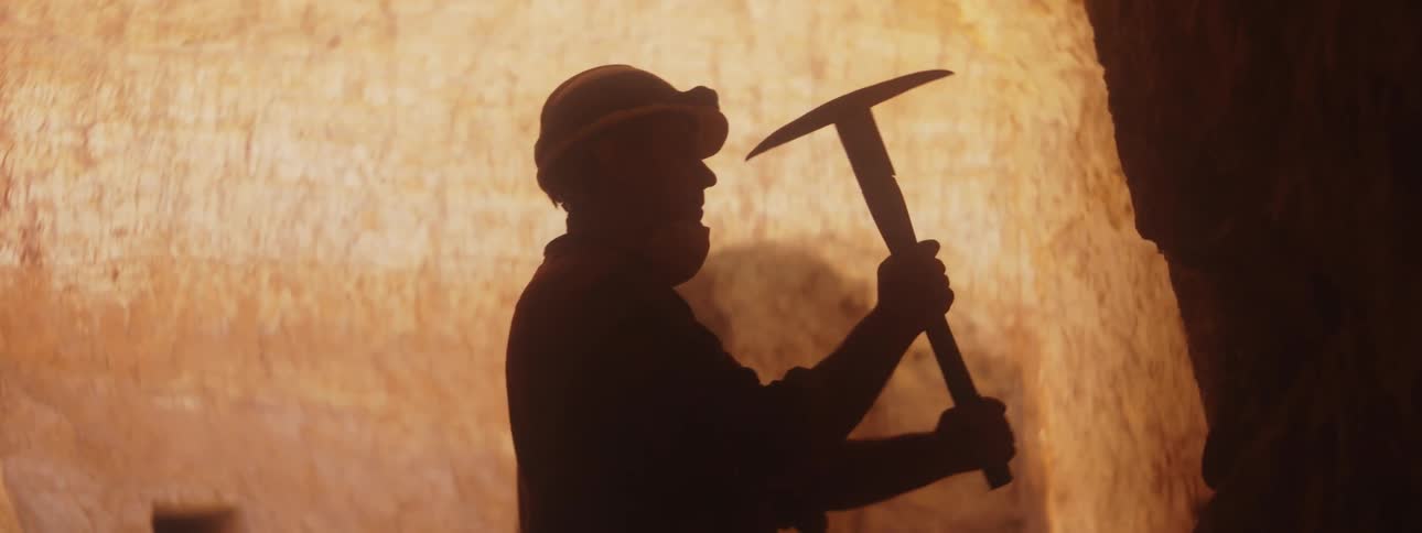 Man silhouetted against brightly lit wall mines with a pickax