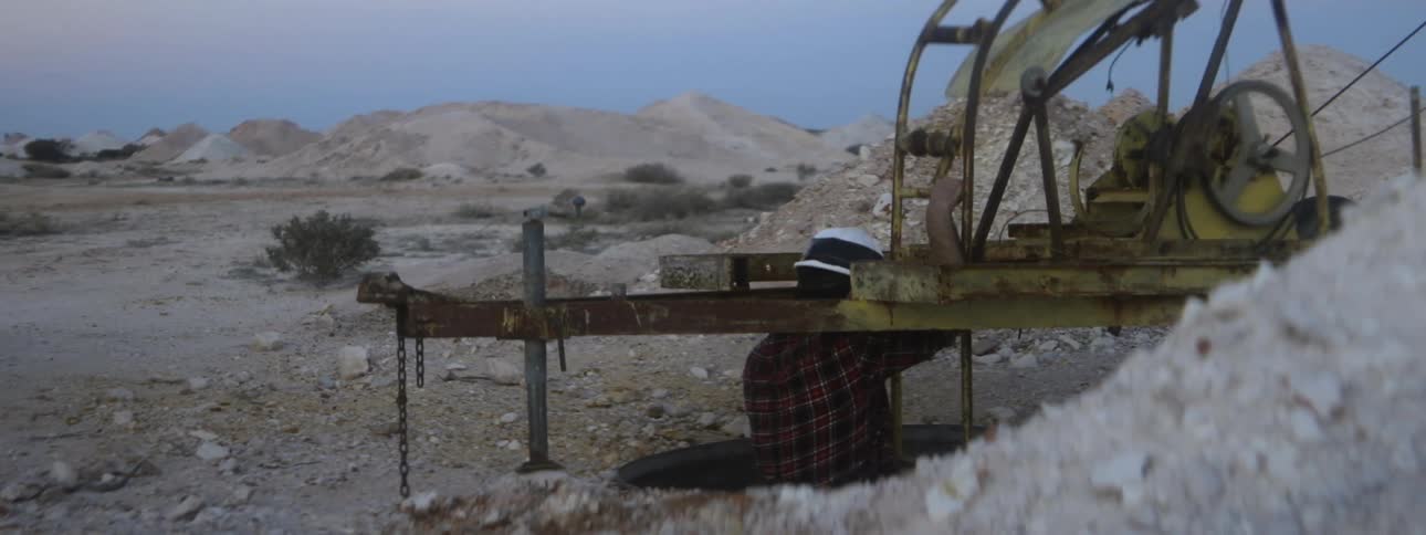 Lone miner climbs down ladder into mine in desert near hills