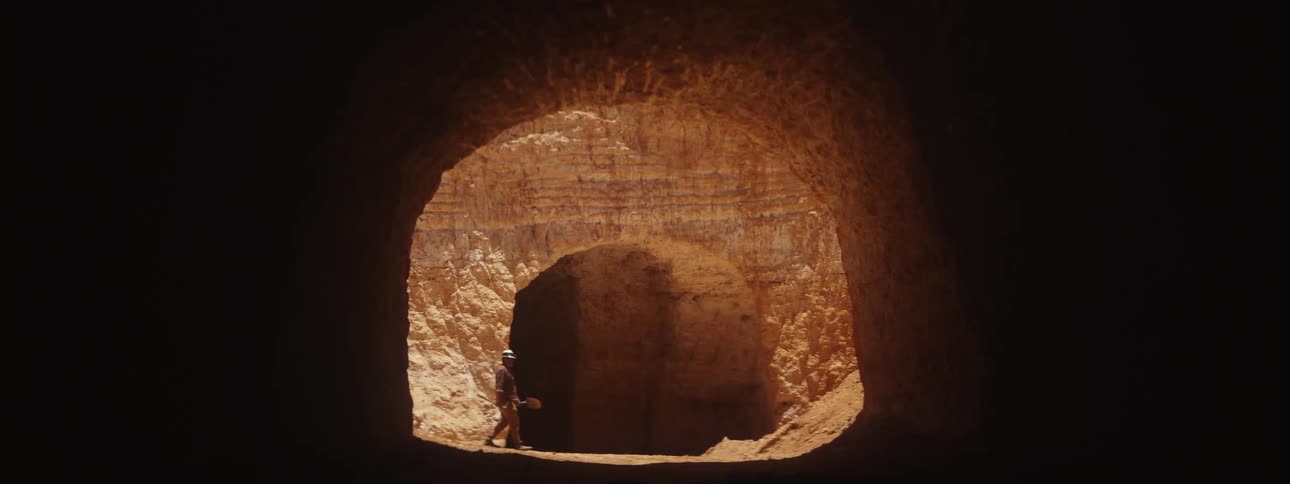 Miner walks through sunlit area between two mine tunnel entrances