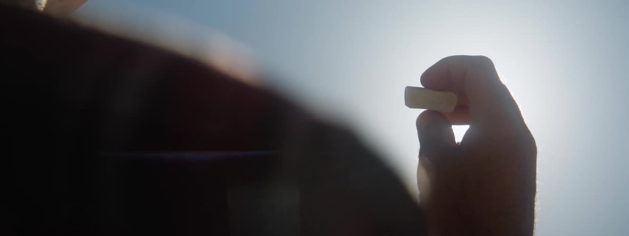 A person is holding a flat rectangular shaped opal as the sun shines brightly in the distance