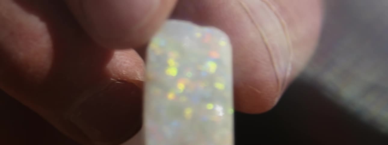 A person is holding a piece of quartz gold ore in their fingers as it sparkles in the sunlight