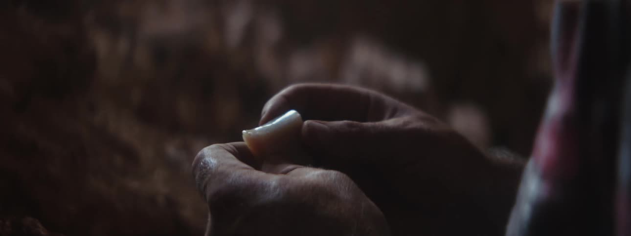 A man inspects a piece of quarts spinning and rotating it on his hands on a dimly lit area
