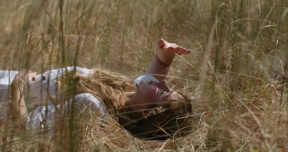 A woman uses her hand to shield her eyes from the sun while lying in a field